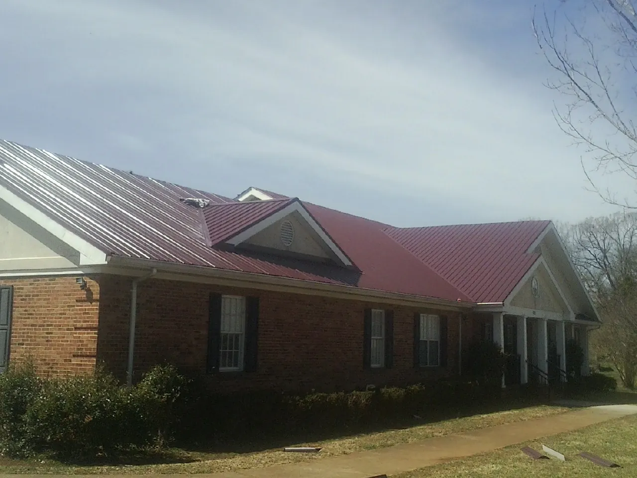Red metal roof with gabled entries on a long brick building, from a Hail Damage Roof Repair job in Suffolk