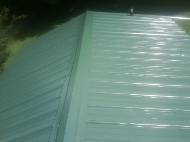 New green metal panels meeting at the ridge of a roof — Flat Roof Repair work by our crew in Suffolk