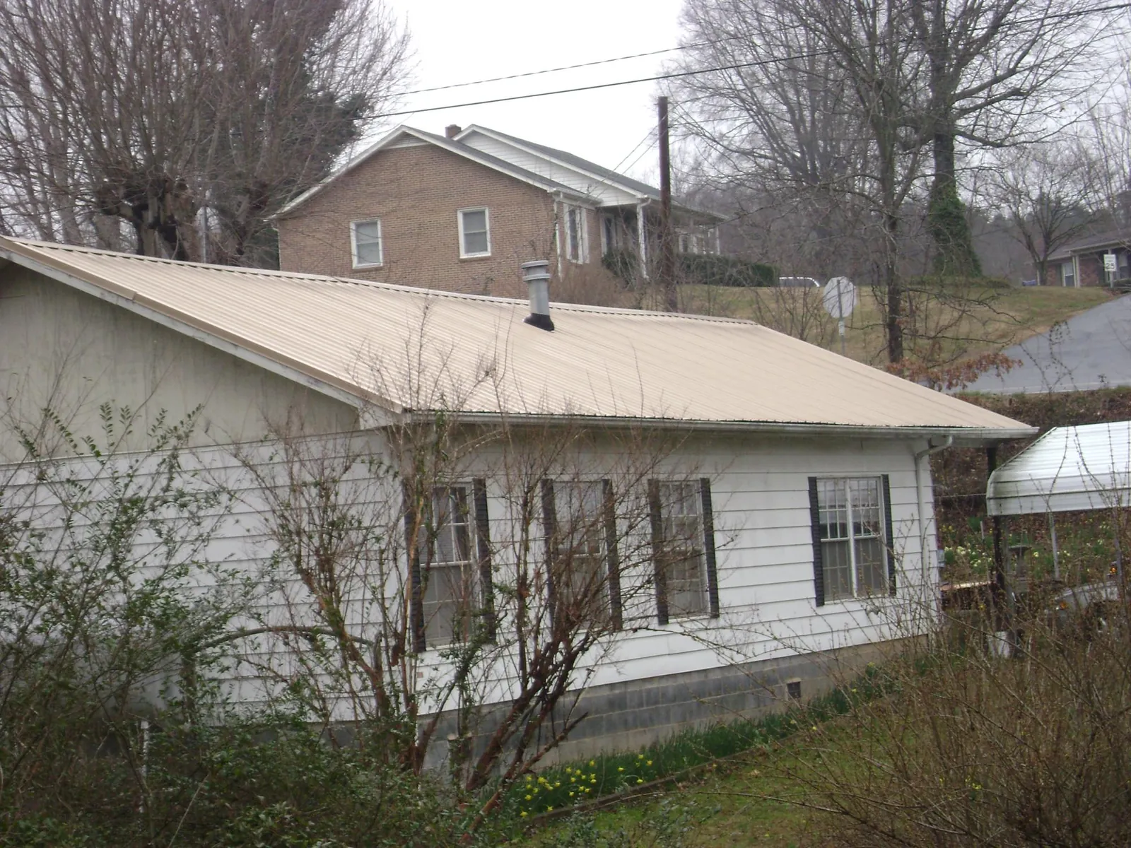 Tan metal roof on a white sided house set into a hillside — Commercial Roofing by Roofing Brothers in Suffolk