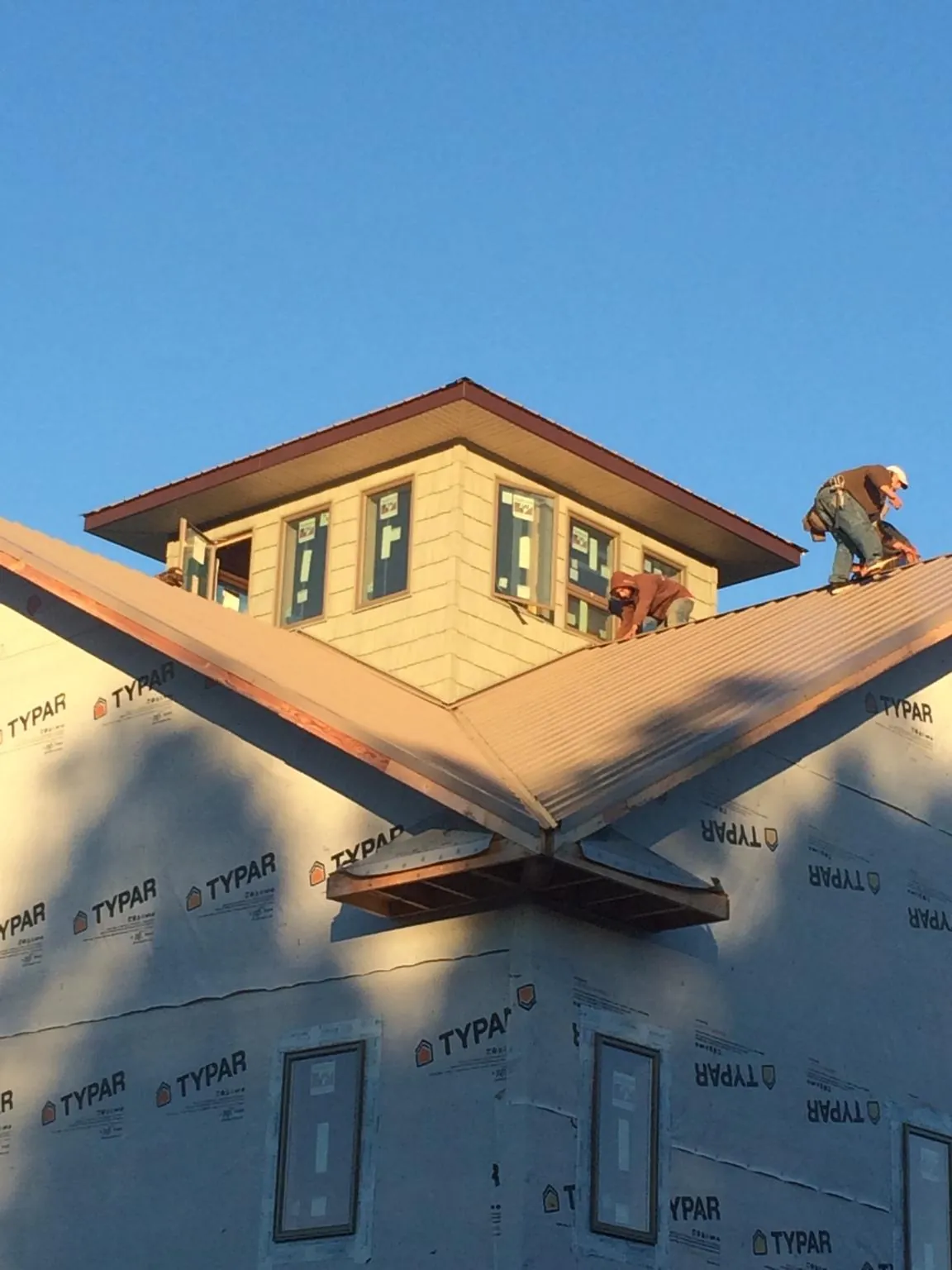 Roofers working around a rooftop cupola on a new metal roof at sunset — Roof Waterproofing in Suffolk by Roofing Brothers